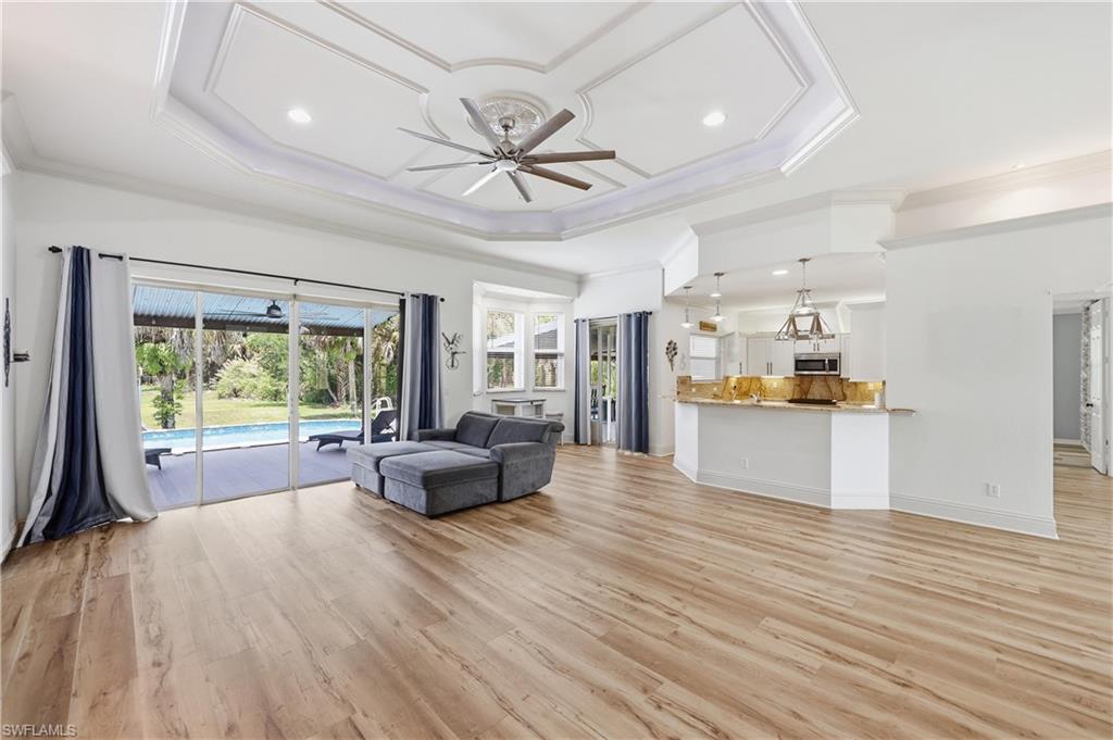 Bright room with tray ceiling detail, wood-look flooring, and large arched window for natural light.