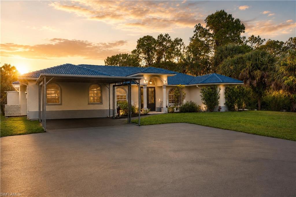 Front exterior featuring a paved driveway, covered parking area, and mature landscaping.