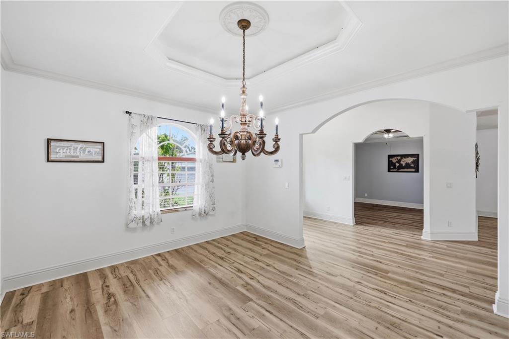 Formal dining room with tray ceiling, decorative chandelier, and arched openings to adjacent living spaces.