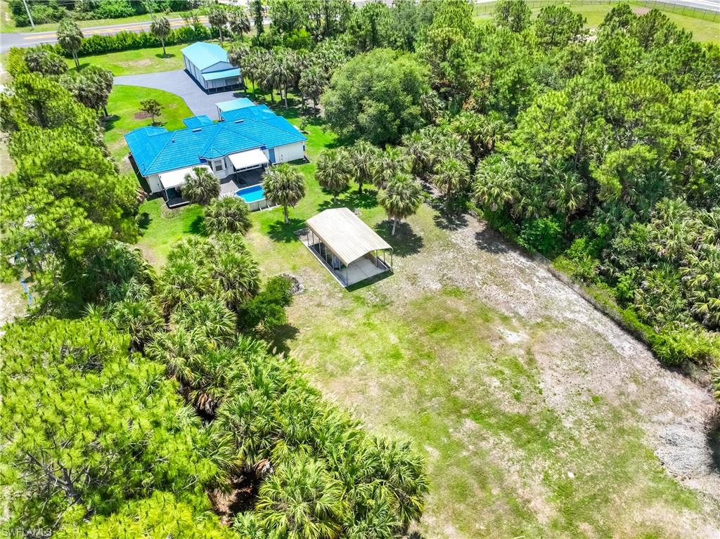 Rear aerial view showcases the pool, backyard, covered parking structure, and mature trees.