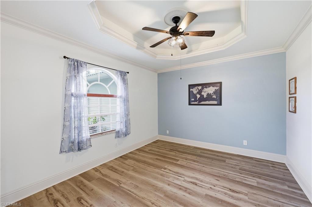 Bright room with tray ceiling detail, wood-look flooring, and large arched window for natural light.