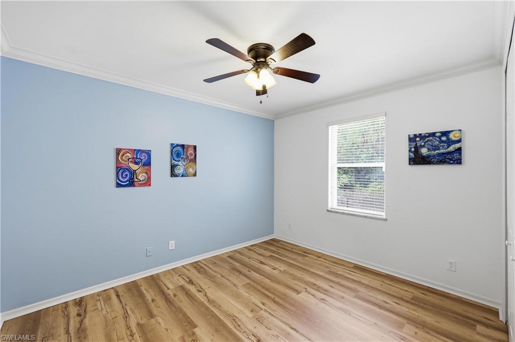 Guest bedroom offering wood-look flooring, ceiling fan, and natural light from a large window.