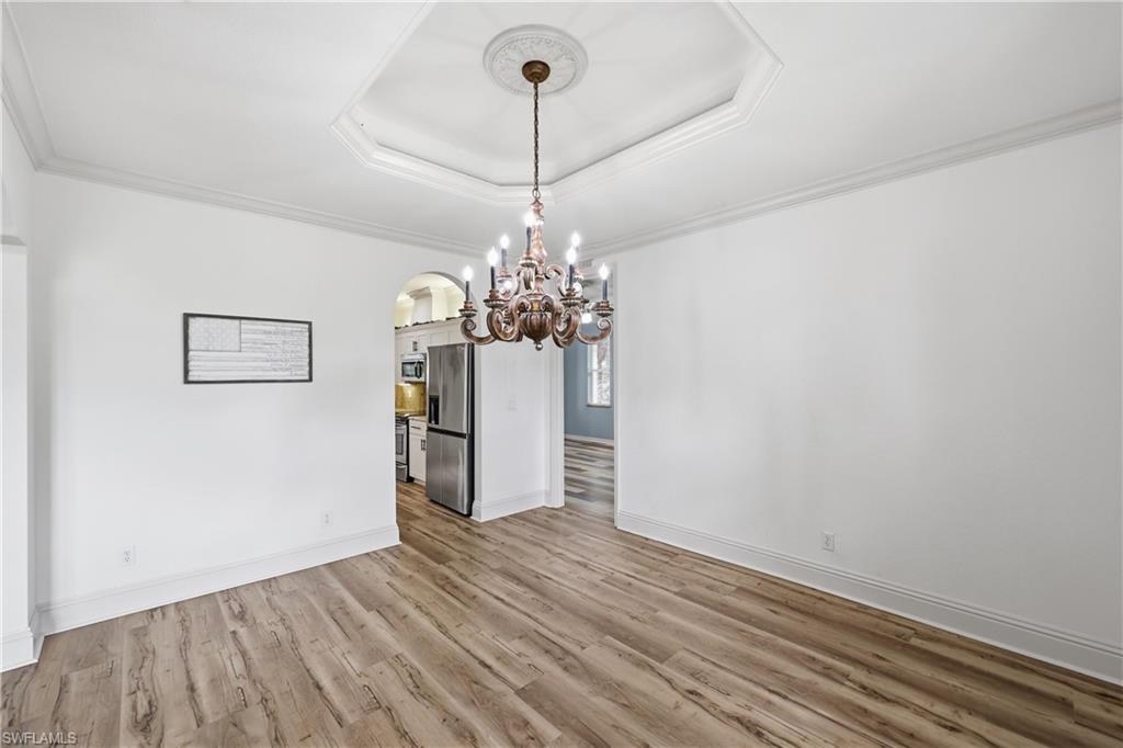 Formal dining room featuring a tray ceiling, decorative chandelier, and wood-look flooring.