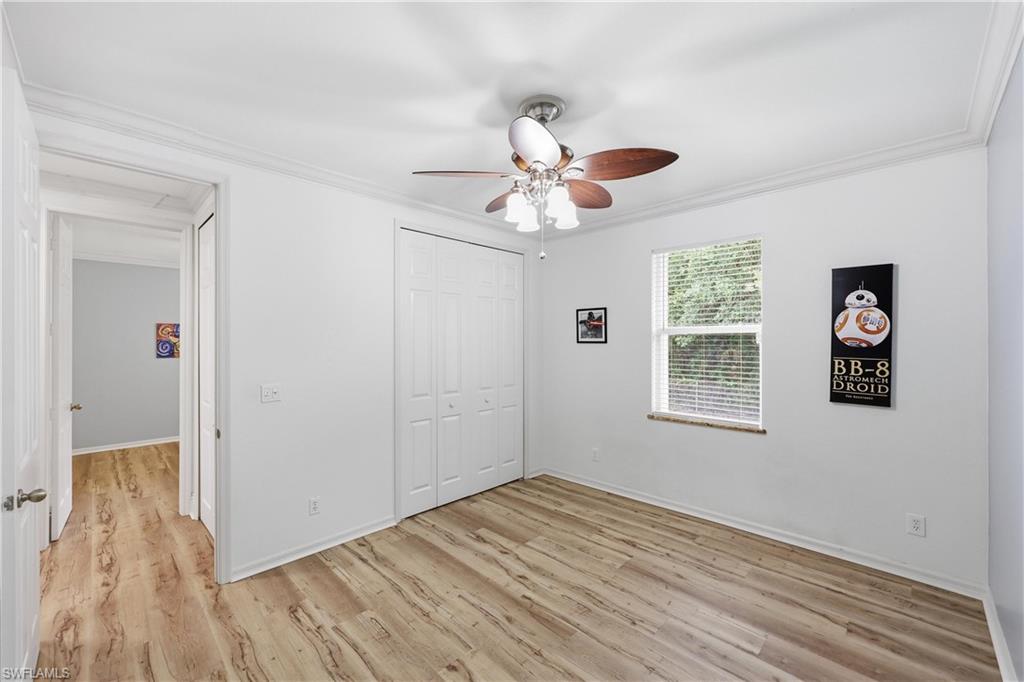 Guest bedroom offering wood-look flooring, ceiling fan, closet storage, and a large window.