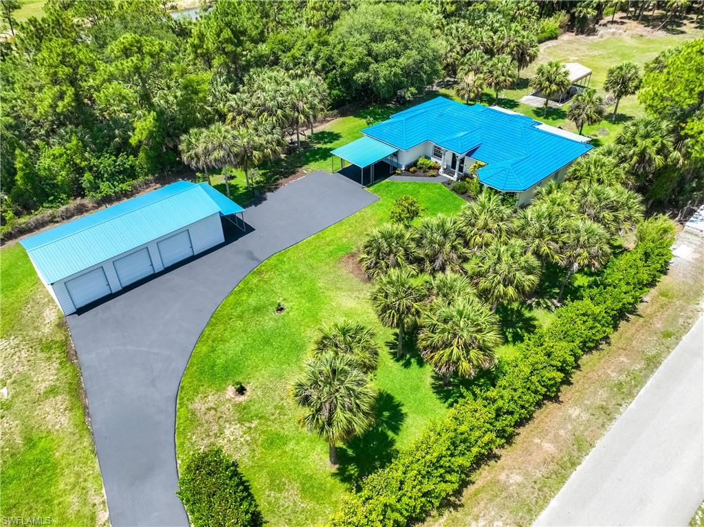 Aerial view highlights the home, detached steel garage, circular driveway, and beautifully landscaped grounds.