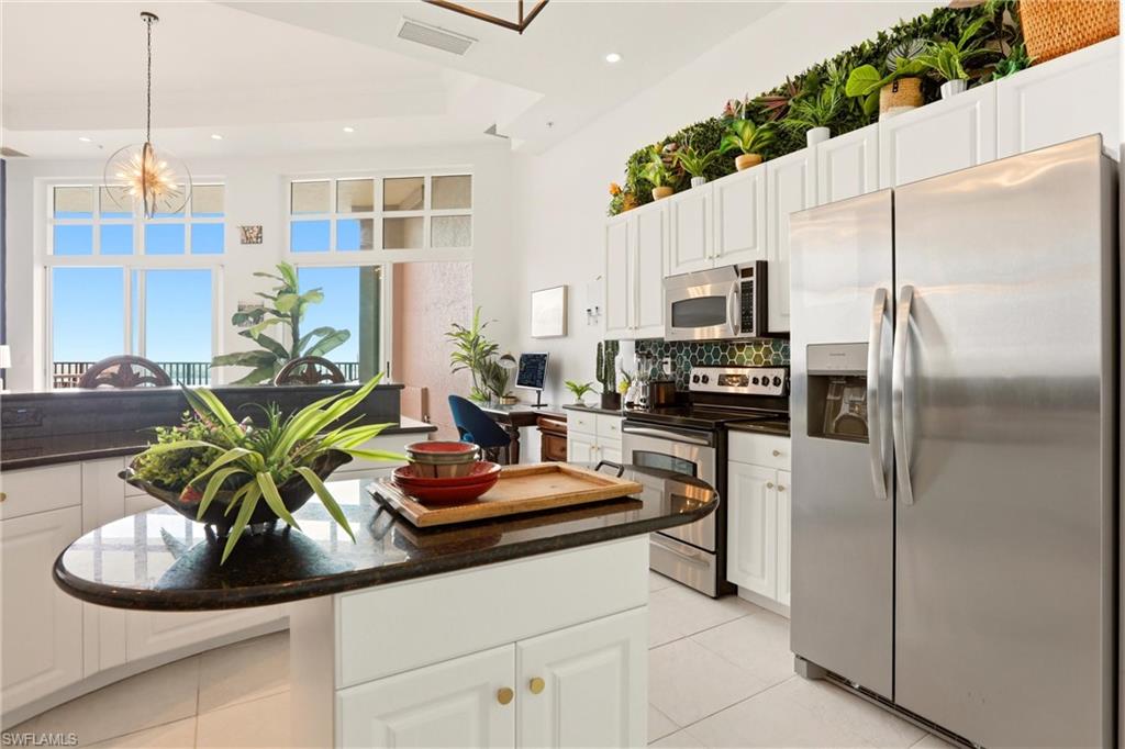 Kitchen featuring stainless steel appliances, white cabinetry, a kitchen island, dark stone counters, and hanging light fixtures
