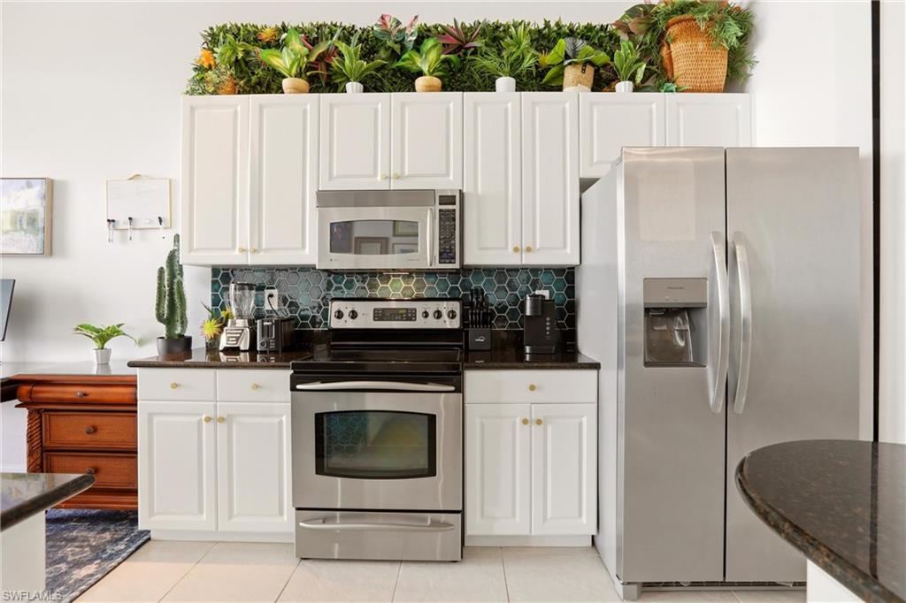 Kitchen with stainless steel appliances, dark stone counters, white cabinetry, and backsplash
