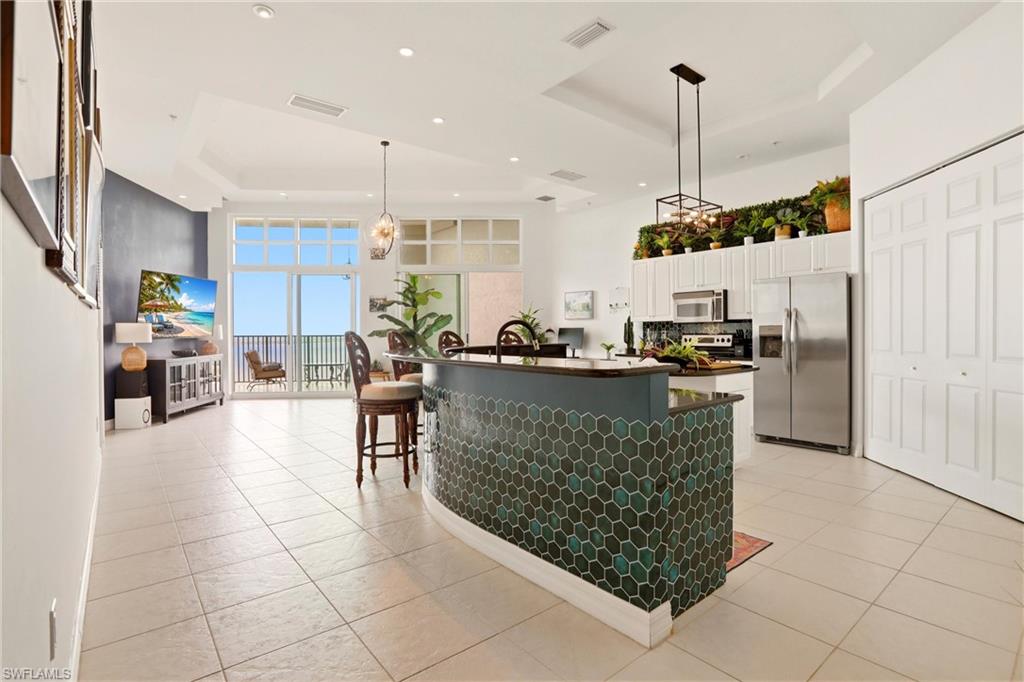 Kitchen with stainless steel appliances, a tray ceiling, white cabinets, a large island with sink, and a kitchen breakfast bar