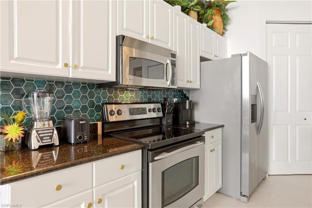 Kitchen with stainless steel appliances, white cabinetry, dark stone countertops, tasteful backsplash, and light tile patterned floors