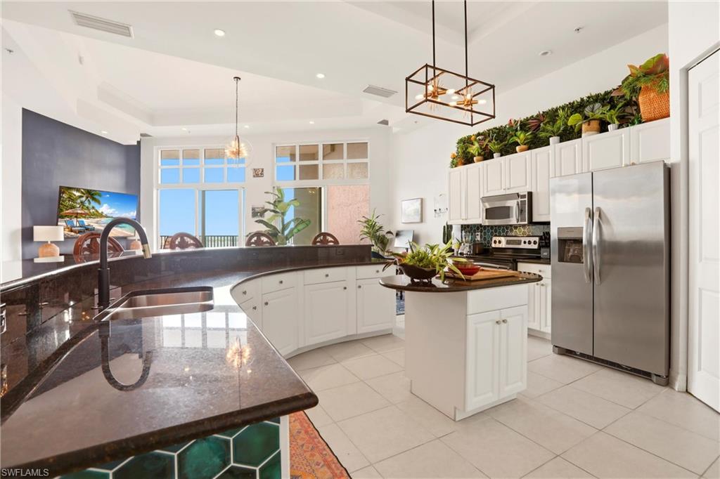 Kitchen featuring stainless steel appliances, white cabinetry, tasteful backsplash, hanging lights, and a high tray ceiling