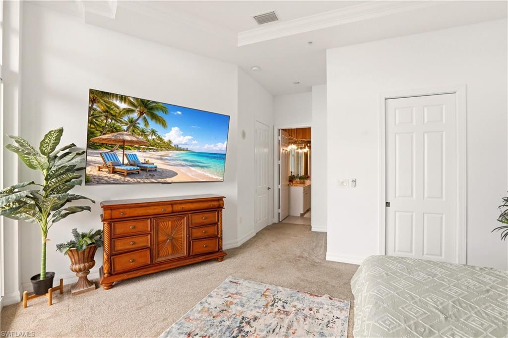 Bedroom with light colored carpet, ornamental molding, connected bathroom, and a tray ceiling