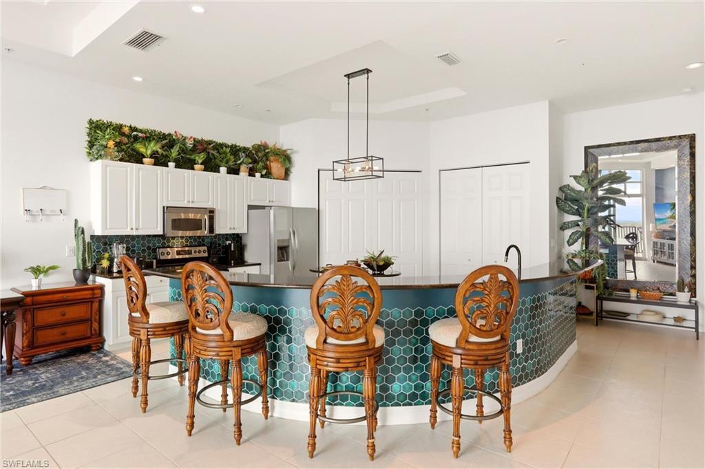 Kitchen with a breakfast bar area, stainless steel appliances, white cabinetry, a large island with sink, and dark stone countertops
