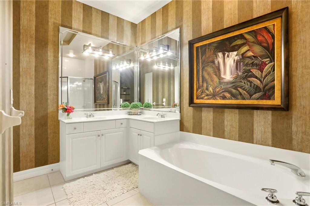 Full bathroom with wallpapered walls, double vanity, light tile patterned flooring, and a bath
