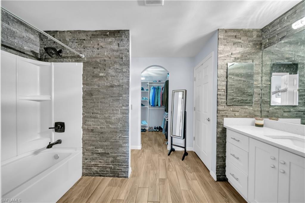 Bathroom featuring vanity, light wood-type flooring, a spacious closet, and shower / bathtub combination