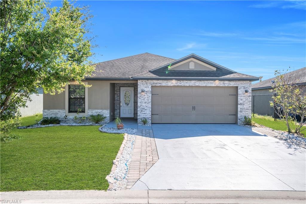 Single story home with a front lawn, an attached garage, concrete driveway, stone siding, and roof with shingles