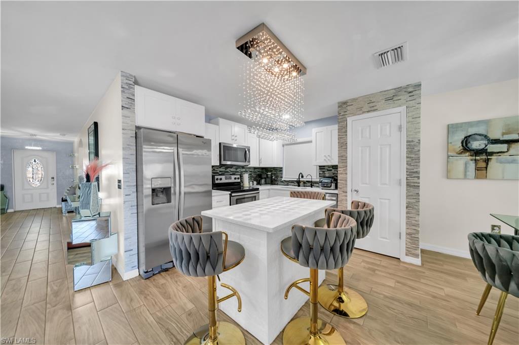 Kitchen featuring stainless steel appliances, suspended lighting, light wood-style floors, and white cabinetry