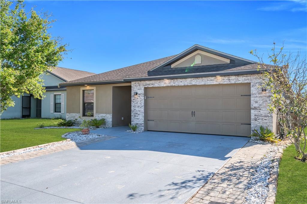 Ranch-style home with a front lawn, concrete driveway, stucco siding, an attached garage, and stone siding