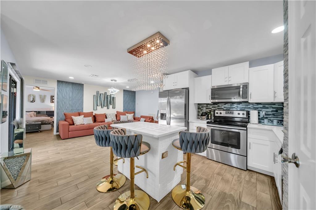 Kitchen with stainless steel appliances, a center island, white cabinets, hanging lights, and open floor plan