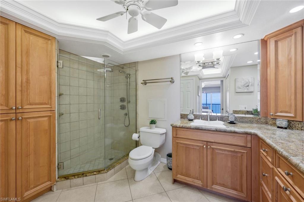 Bathroom featuring crown molding, a tray ceiling, a shower with shower door, vanity, and toilet