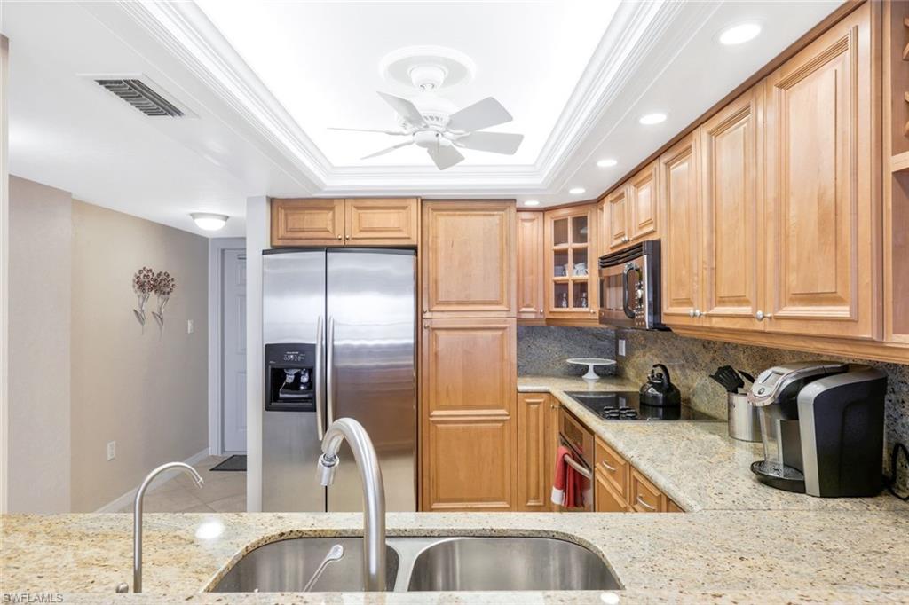 Kitchen featuring ceiling fan, tasteful backsplash, a raised ceiling, light stone counters, and appliances with stainless steel finishes