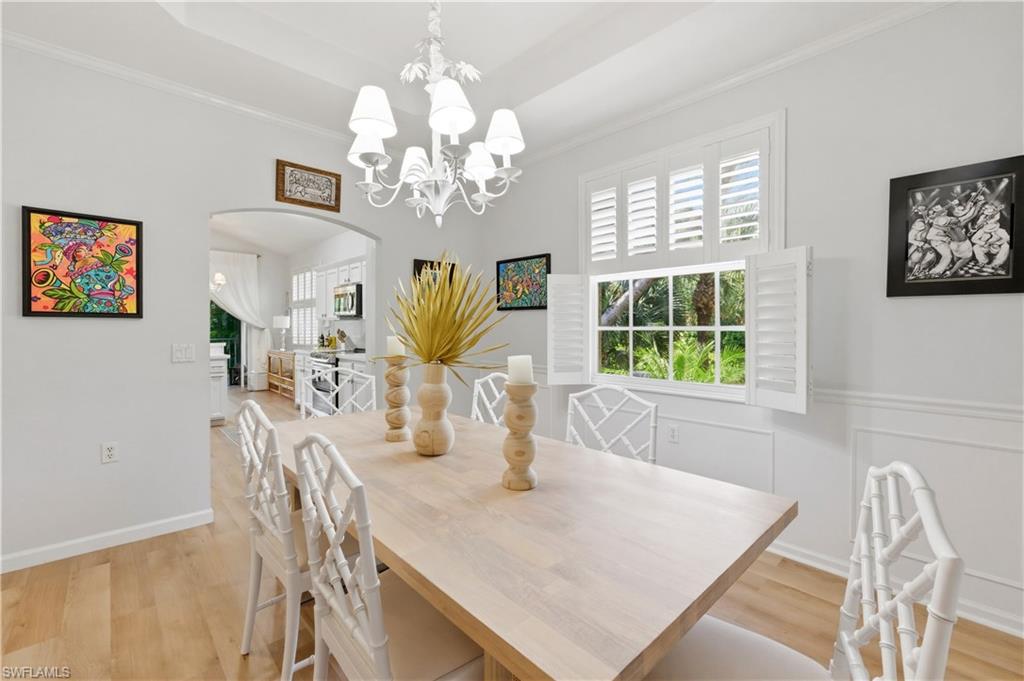 Dining room featuring arched walkways, light wood-type flooring, suspended lighting, crown molding, and a raised ceiling