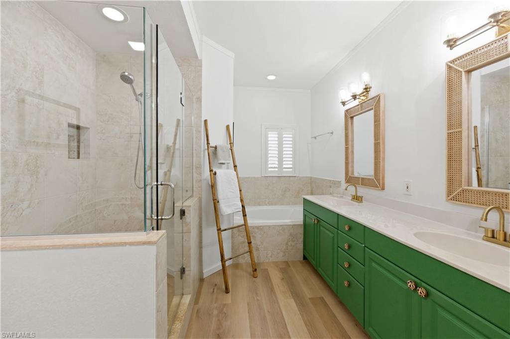 Bathroom with a bath, light wood-type flooring, double vanity, a stall shower, and ornamental molding
