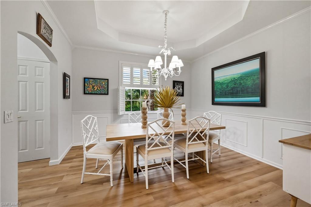 Dining area with crown molding, a chandelier, arched walkways, light wood-style floors, and a tray ceiling