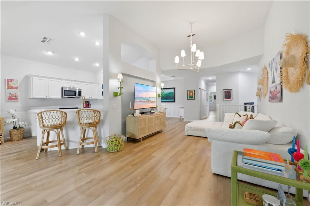 Living room with light wood finished floors, suspended lighting, and a high ceiling