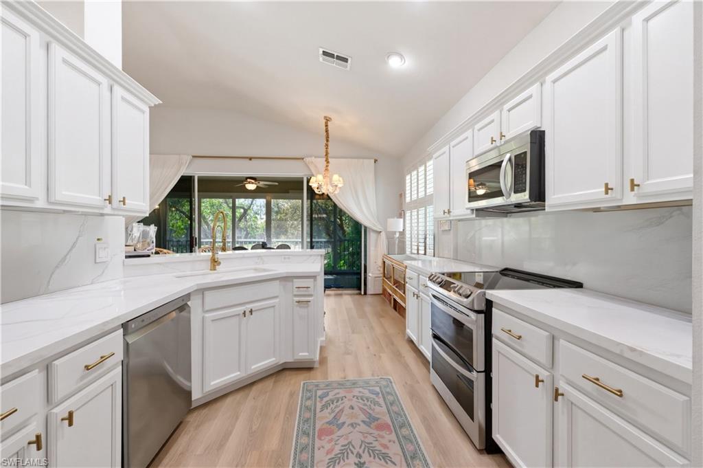 Kitchen featuring stainless steel appliances, lofted ceiling, white cabinets, a peninsula, and light wood-style flooring
