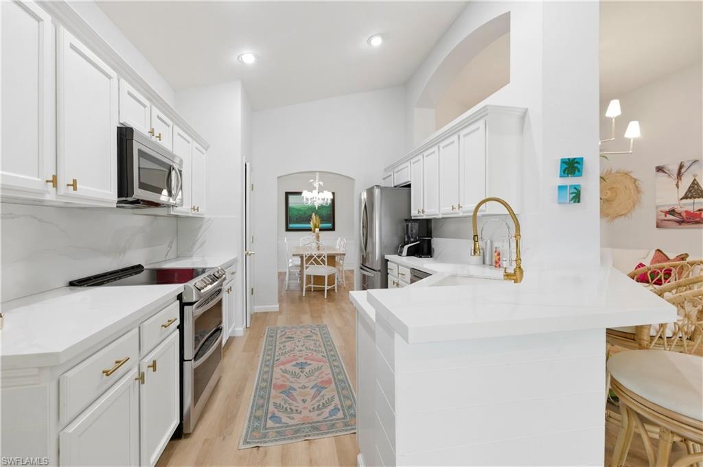 Kitchen featuring stainless steel appliances, a peninsula, arched walkways, light wood finished floors, and white cabinets