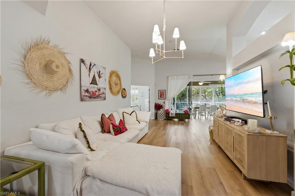 Living room featuring light wood-type flooring, hanging lights, and vaulted ceiling