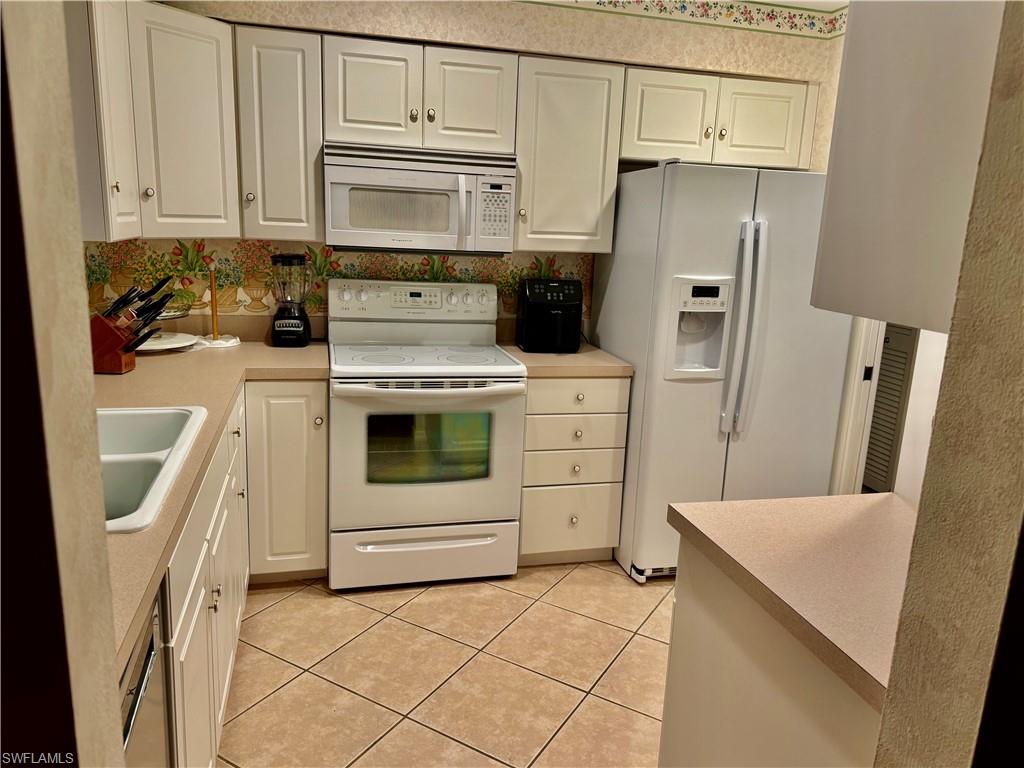 Kitchen featuring white appliances, light countertops, light tile patterned flooring, and white cabinets