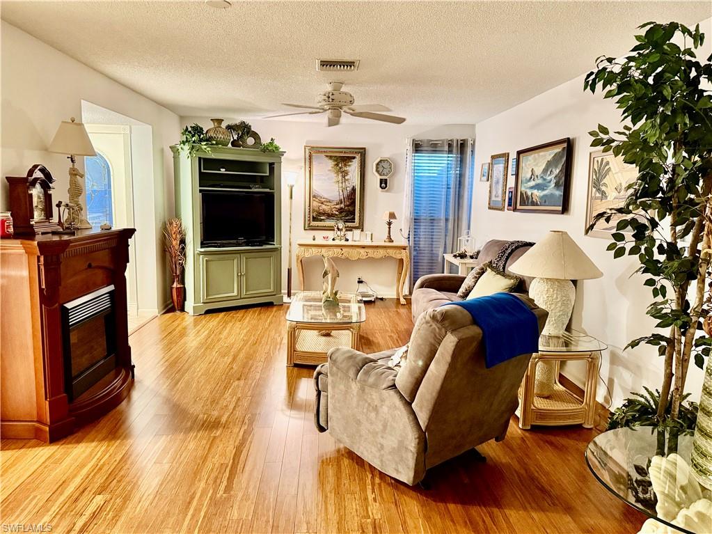 Living area featuring light wood-style flooring, a textured ceiling, a fireplace, and ceiling fan