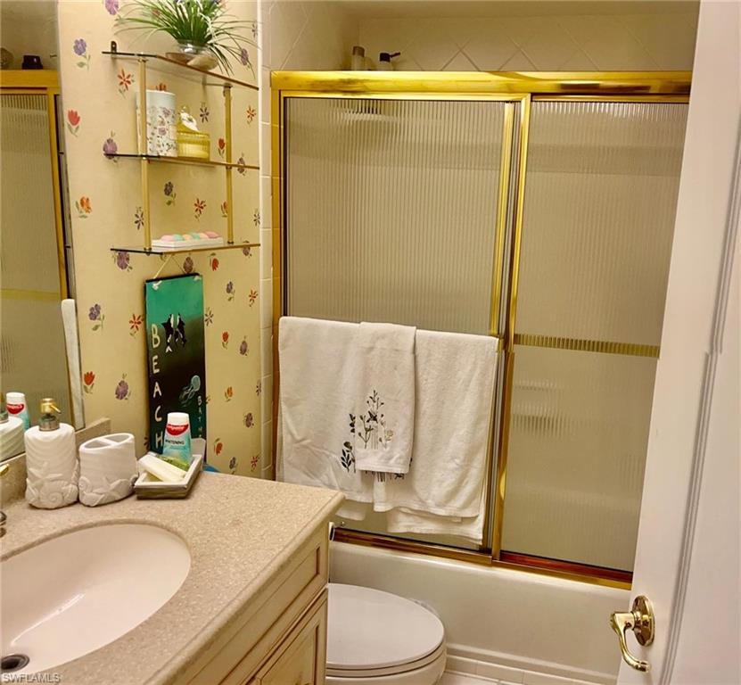 Full bath with vanity, toilet, and shower / bath combination with glass door