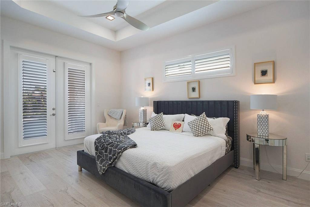 Bedroom with access to exterior, a raised ceiling, light wood-type flooring, and a ceiling fan