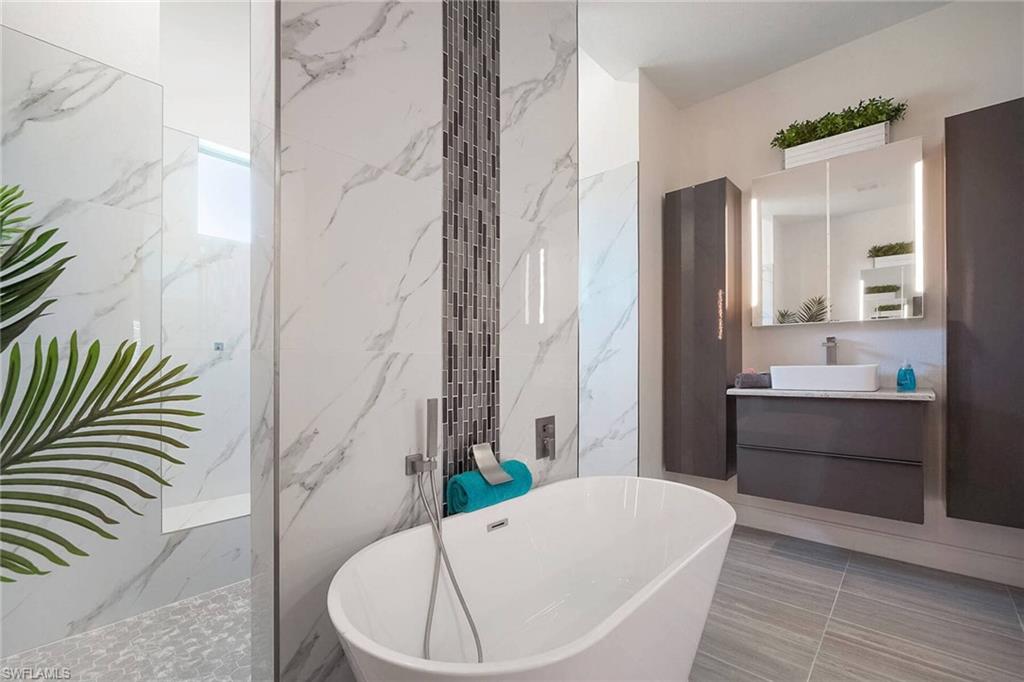 Bathroom with vanity, a marble finish shower, a freestanding bath, tile walls, and stone wall
