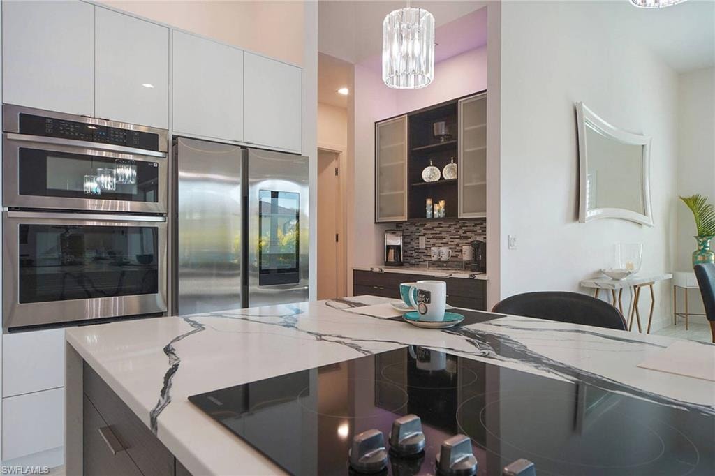 Dual tone kitchen with modern cabinets, stainless steel appliances, glass fronted cabinets, tasteful backsplash, and light stone counters