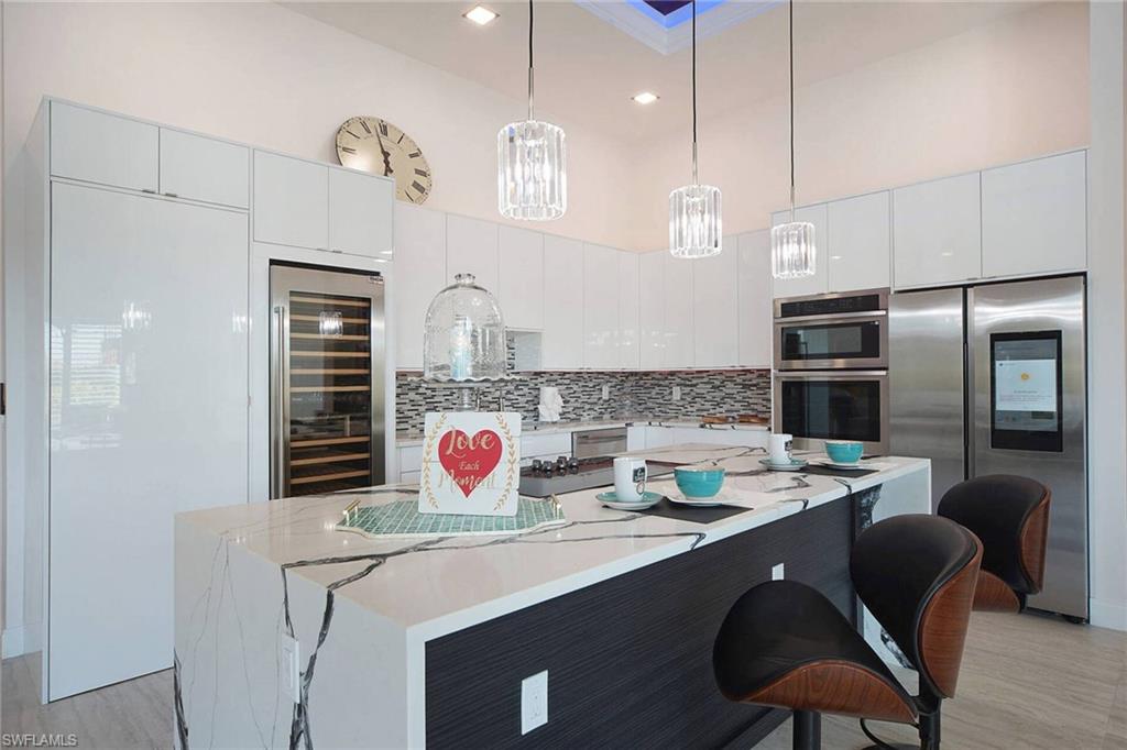 Kitchen featuring stainless steel appliances, a center island, white cabinetry, a kitchen bar, and beverage cooler