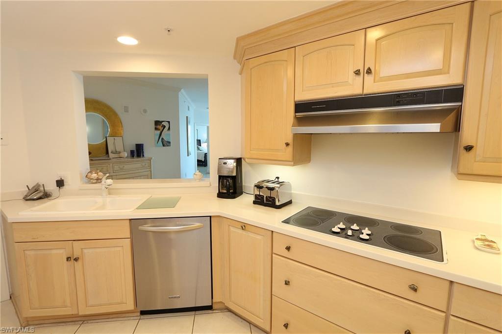 Kitchen featuring black electric cooktop, under cabinet range hood, dishwasher, light brown cabinets, and a sink
