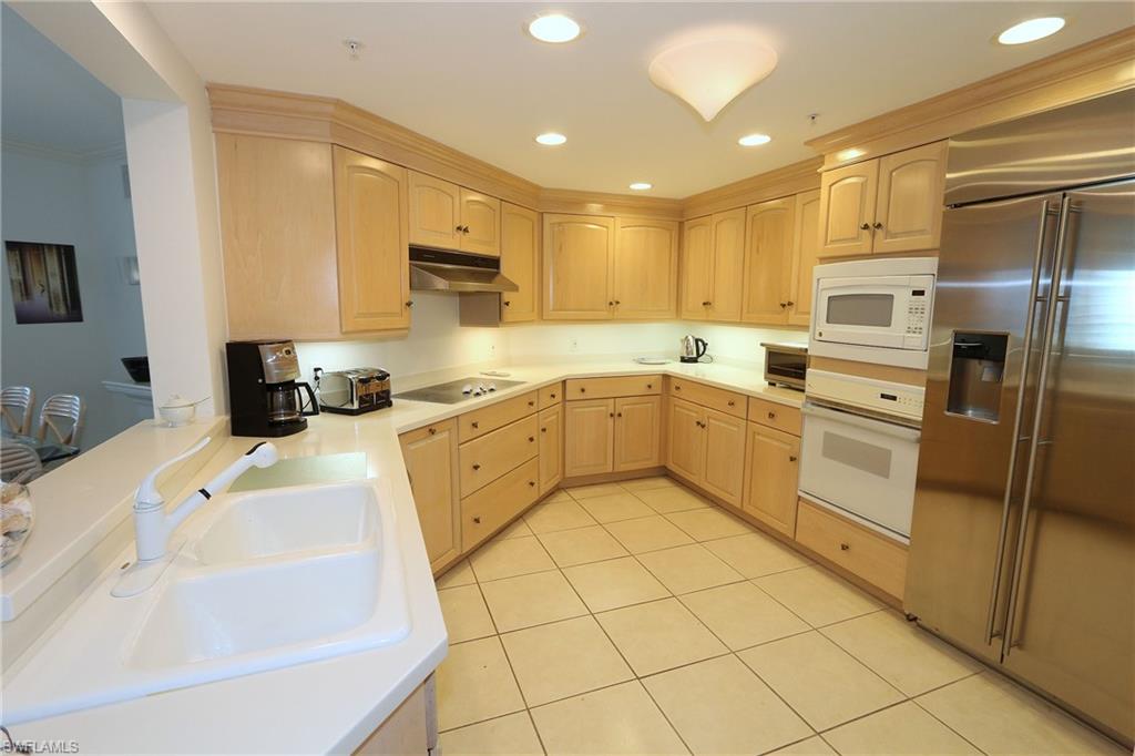 Kitchen featuring light brown cabinetry, a sink, white appliances, under cabinet range hood, and light tile patterned floors