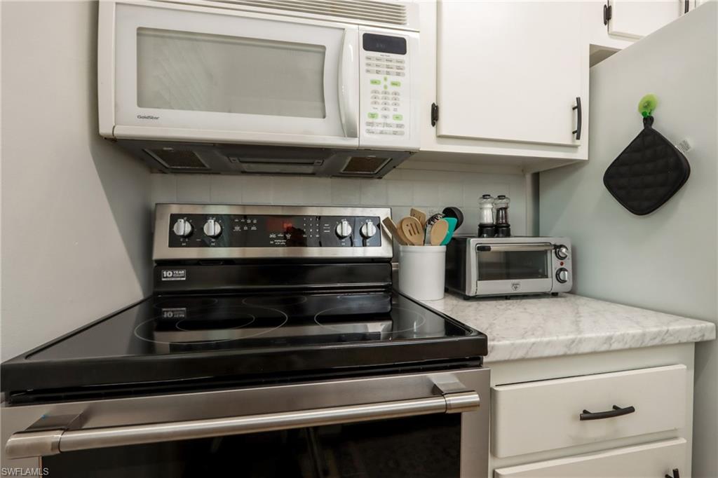 Kitchen featuring stainless steel range with electric stovetop, white microwave, tasteful backsplash, and white cabinetry