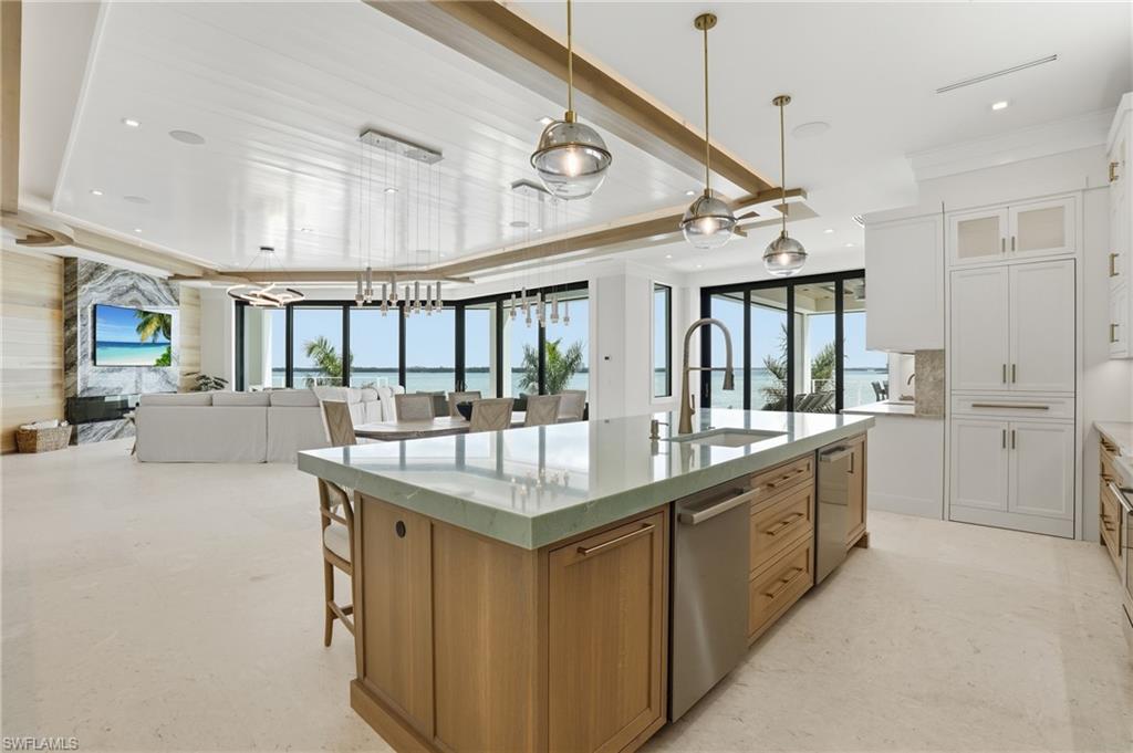 Kitchen with two tone color scheme, open floor plan, a large island with sink, light stone countertops, and pendant lighting - Virtually Edited Image