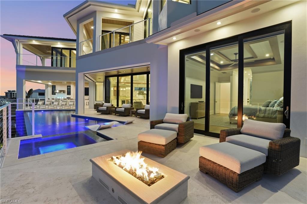 Rear view of property featuring a balcony, a patio, an outdoor living space with a fire pit, stucco siding, and a pool with connected hot tub - Virtually Edited Image