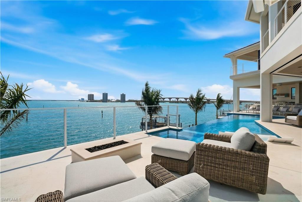 View of swimming pool with a water view, an outdoor living space with a fire pit, an infinity pool, and patio surround - Virtually Edited Image