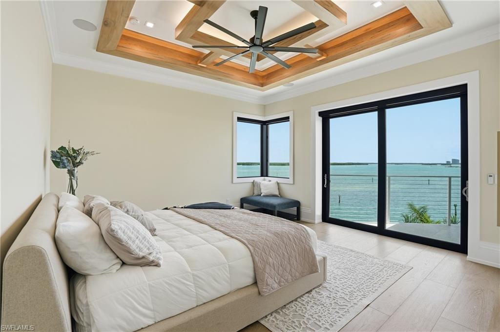 Bedroom featuring a water view, access to exterior, light wood-style floors, a ceiling fan, and ornamental molding - Virtually Edited Image