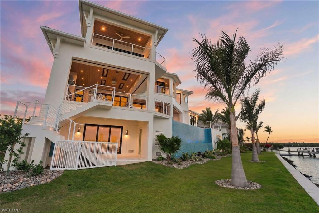 Back of house at dusk featuring a balcony, a patio, stucco siding, and a yard - Virtually Edited Image