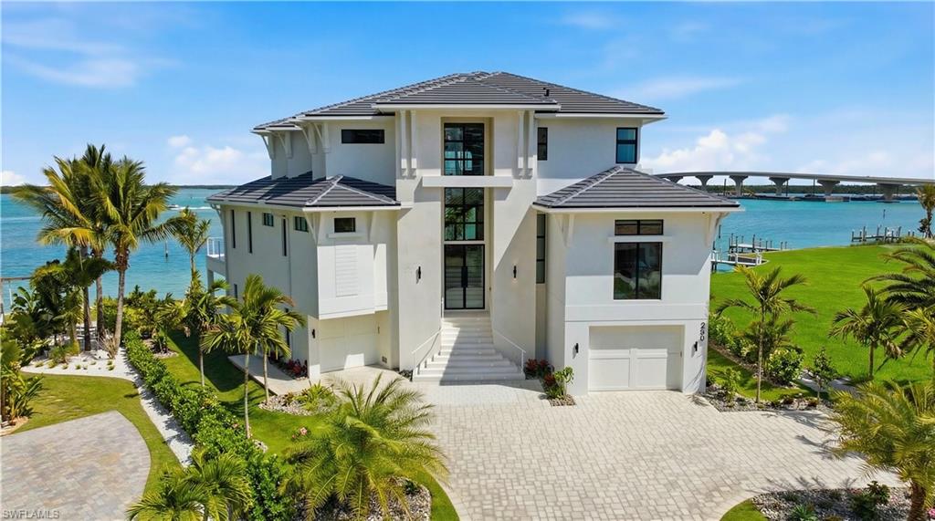View of front facade featuring a water view, a tile roof, a garage, and decorative driveway - Virtually Edited Image
