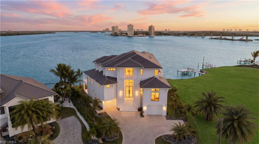 View of front of house featuring a water view, decorative driveway, stucco siding, a view of city, and an attached garage - Virtually Edited Image