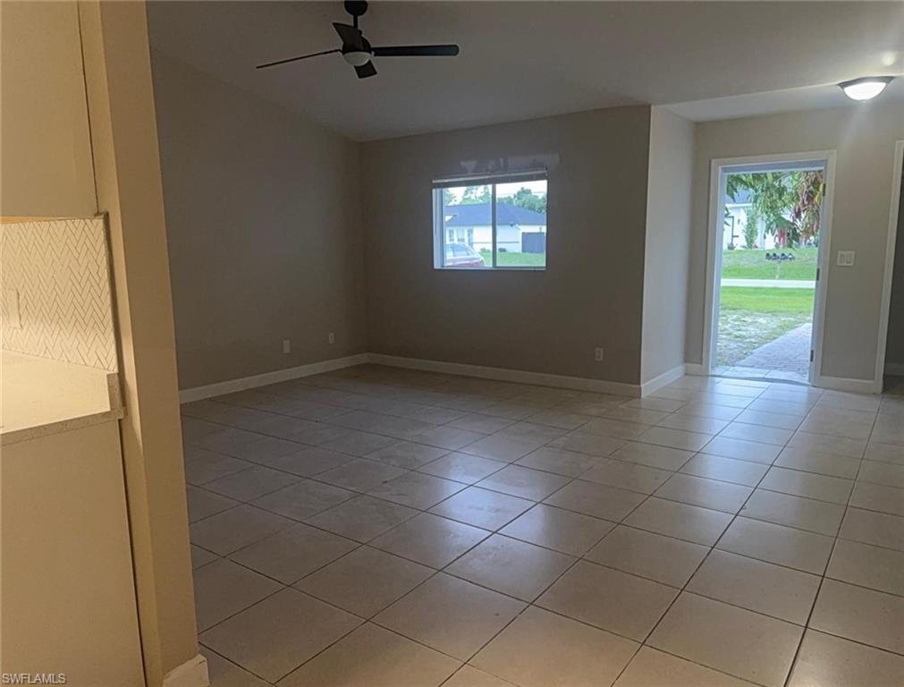 Spacious living area featuring neutral-toned walls, square tile flooring, and a modern ceiling fan
