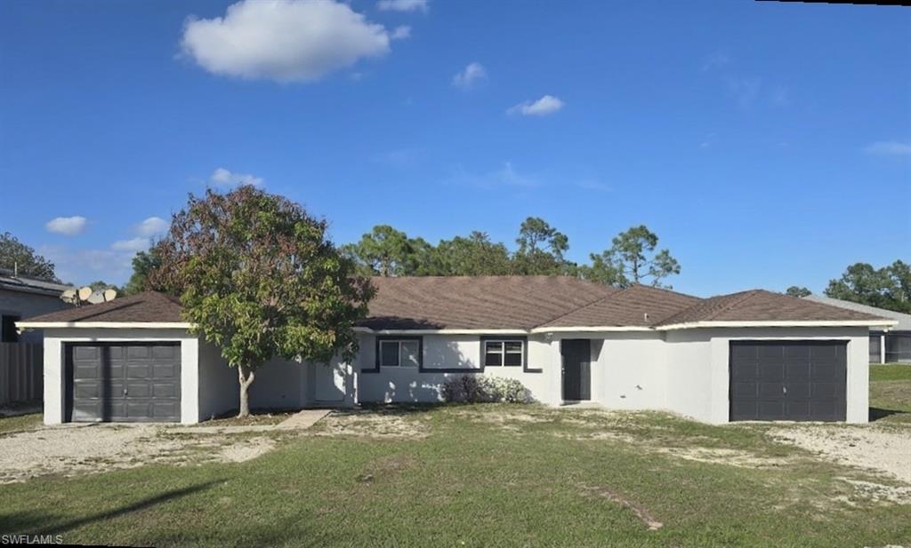 home with an attached garage, driveway, stucco siding, and a front yard